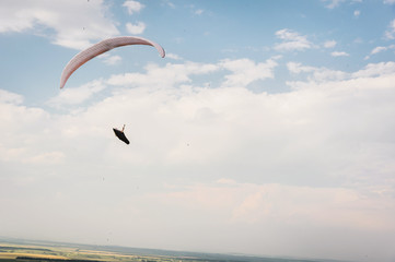 A white-orange paraglider flies over the mountainous terrain