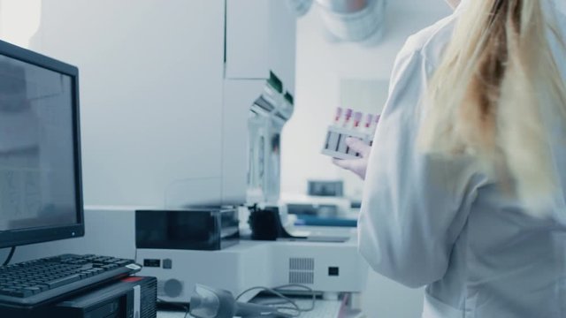 Female Research Scientist Takes Test Tubes with Blood Samples and Puts them into Analyzer Medical Machine. Scientist Works with Modern Medical Equipment in Pharmaceutical Laboratory.