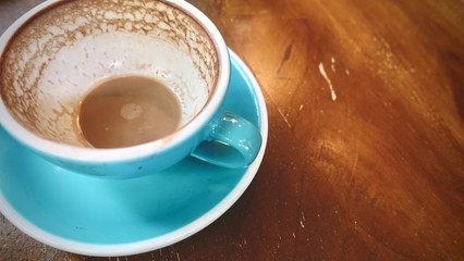 close up, finished cup of hot cappuccino or hot latte coffee with leftover latte art, put on natural brown wooden board table in cafe, coffee lover concept     
