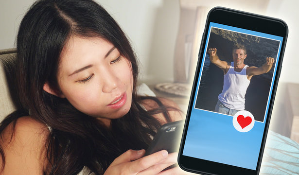 young beautiful and happy Asian Korean woman using internet online dating app on mobile phone sending like message to handsome Caucasian man searching for love