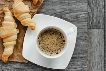 Four croissants and coffe on a wooden light cutting board on a wooden tabletop.