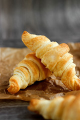 Four croissants and coffee on a wooden light cutting board on a wooden tabletop.