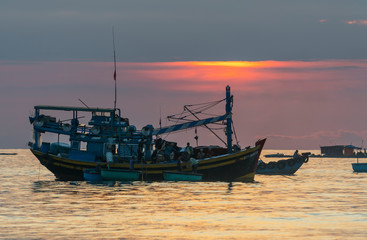 Fototapeta premium Mui Ne, Vietnam - September 28, 2018: Sea view at dawn when sunrise horizon, fishermen transport sea fish from the boat to shore trade for their family in coastal fishing village in Mui Ne, Vietnam