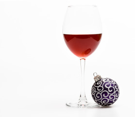 Winter holidays concept. Winter celebration with alcohol drink. Glass with wine and christmas decoration. Wineglass with red liquid or wine and christmas ball ornament isolated on white background