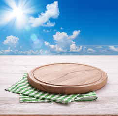 Wooden deck table with tablecloth over summer sky and sun background