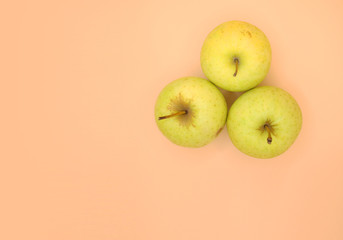 Three golden green apples on light orange surface