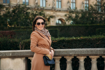 Stylish girl in coat posing for photographer near big park. sunny weather and beautiful model