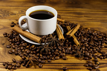Cup of coffee, roasted coffee beans, star anise and cinnamon sticks on wooden table