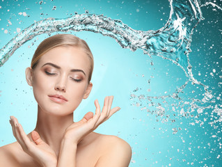 Naklejka premium Beautiful woman with splashes of water in her hands. Beautiful girl under splash of water with fresh skin on blue background. Skin care, cleansing and moisturizing concept. Beauty face