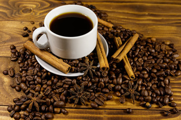 Cup of coffee, roasted coffee beans, star anise and cinnamon sticks on wooden table