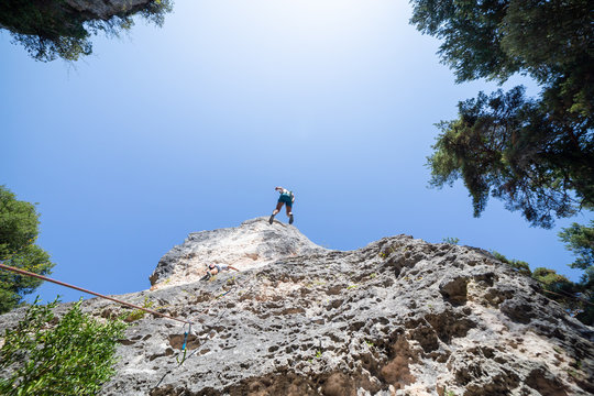 From below shot of climber secured with rope jumping from top of mountain under blue sky while other is climbing 