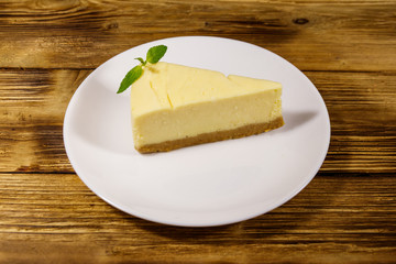 Piece of tasty sweet New York cheesecake in a white plate on wooden table
