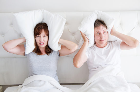 Caucasian middle age family couple angry shouting in bed. Conflict relationship concept. Husband and wife cover ears by pillow. Selective focus