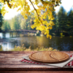 Pizza boapd and napkin on table over blurred trees and river as background, product display template. Selective focus.