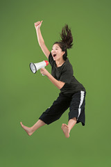 Beautiful young woman jumping with megaphone isolated over green background. Runnin girl in motion...