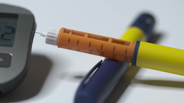 Diabetes testing equipment and insulin therapy. Hyperglycemia. Diabetic pens and glucose meter. High blood sugar level is 11.2 mmol/L 198.20 mg/dL on display of glucometer.