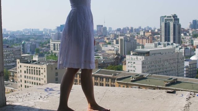 Barefoot woman walks on edge of abandoned building rooftop, reckless daredevil