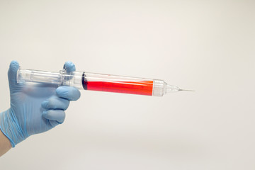 The surgeon's hand in a blue medical glove holds a large syringe with blood . Isolated background.