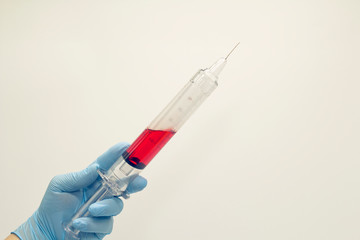 The surgeon's hand in a blue medical glove holds a large syringe with blood . Isolated background.