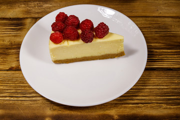 Piece of tasty New York cheesecake with raspberries in a white plate on wooden table