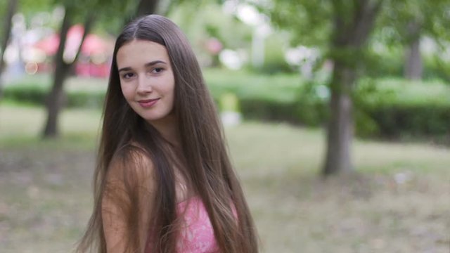 Attractive young woman flips hair turning around in park slow motion outdoors
