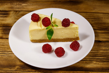 Piece of tasty New York cheesecake with raspberries in a white plate on wooden table