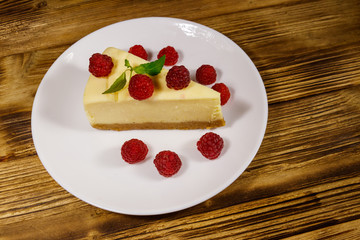 Piece of tasty New York cheesecake with raspberries in a white plate on wooden table