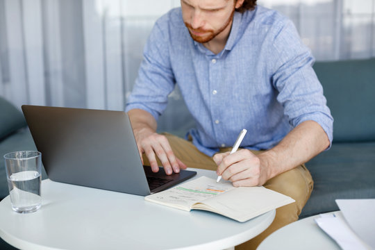 Caucasian ginger serious businessman writing a his notebook and looking at laptop.