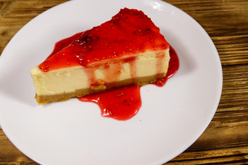 Piece of tasty New York cheesecake with raspberry jam in a white plate on wooden table