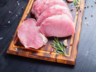 Pork steak, raw carbonate fillet on dark background, meat with rosemary, seasonings, side view.