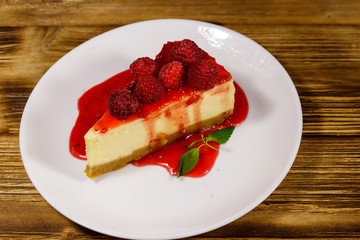 Piece of tasty New York cheesecake with raspberries and raspberry jam in a white plate on wooden table