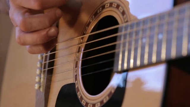 Close up shot of guitarist's hands plays chords on acoustic guitar at home