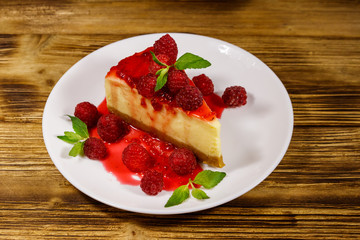 Piece of tasty New York cheesecake with raspberries and raspberry jam in a white plate on wooden table