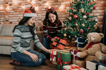 young sisters putting gifts under the xmas tree