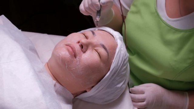 Hardware cosmetology. Relaxed Muslim woman with eyes closed during a therapeutic disincrustation procedure. Asian girl on galvanic cleaning of the skin in the beauty salon.