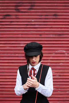 Fashionable woman with red lips wearing black peaked cap standing in front of red roller shutter