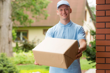 Happy young courier in blue uniform holding a package