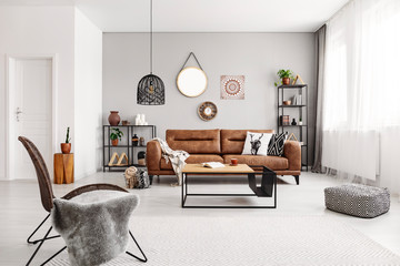 Armchair and pouf near table in grey living room interior with leather sofa and mirror. Real photo