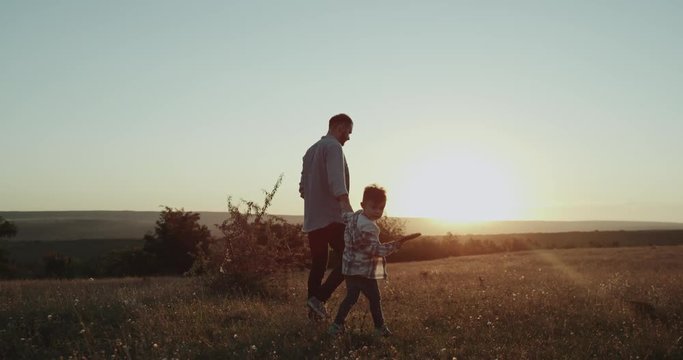 Dad with his boy three years old, at sunset in the middle of field playing with a small racquet for tennis table , running , amazing view.