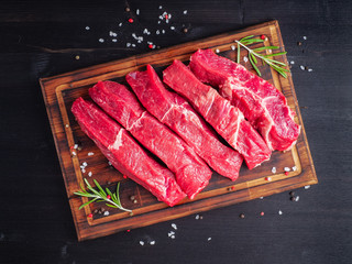 Raw meat, beef steak with seasoning on chopping board on dark background with rosemary, seasonings, top view
