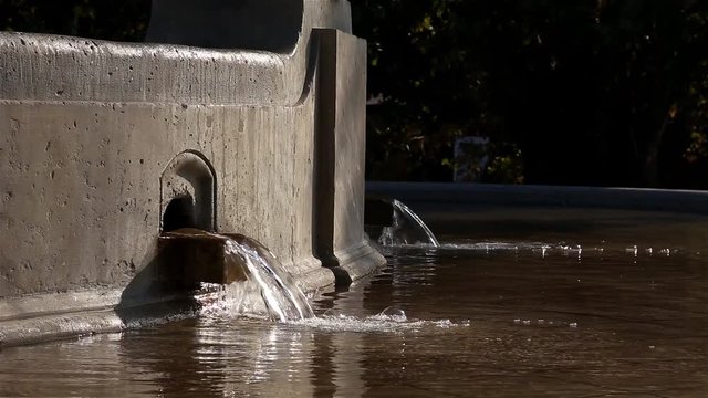 Drops of water pouring from a concrete city fountain close-up.