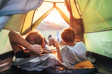 Father and son lie together in touristic tent and enjoy with sunset light - obrazy, fototapety, plakaty