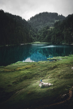 See an einem regnerisch bew&ouml;lkten Tag in den Bergen Taubensee ein Wanderer sitzt auf einem Stein davor 
