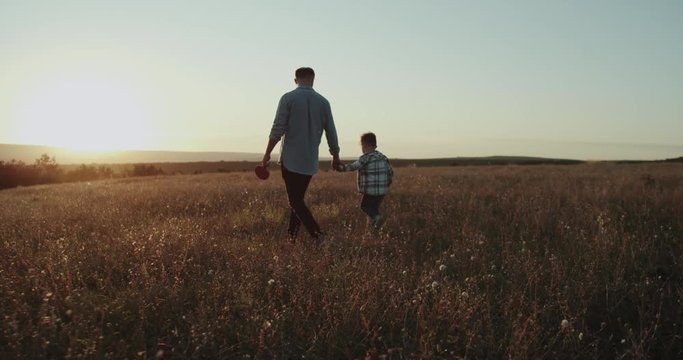 Dad with his boy , at sunset walking through the field, dad holding a racquet of tennis table. shot on red epic. 4k