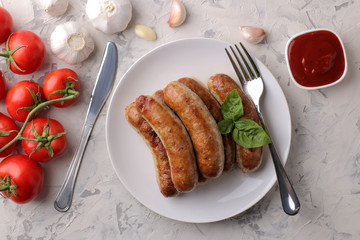 Grilled sausages with a variety of vegetables tomatoes and garlic, red sauce and spices on a light background. top view