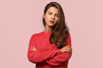 Obraz premium Beautiful long-haired brunette girl crossed her arms on her chest and looks carefully at the camera. Gaze and serious expression
