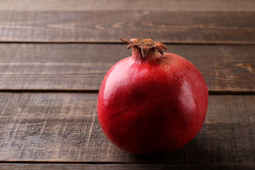 Large ripe red pomegranate fruit on a brown wooden table with space for inscription.