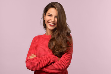 Fototapeta premium Studio isolated portrait of a young beautiful student girl with long dark hair. She smiles warmly and looks into the camera. Her arms folded across her chest
