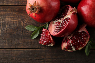 Composition of ripe pomegranate fruit with green leaves on a brown wooden background.