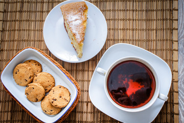 Plum biscuit cake for a cup of hot tea on a straw bedding with chocolate biscuits in a basket.